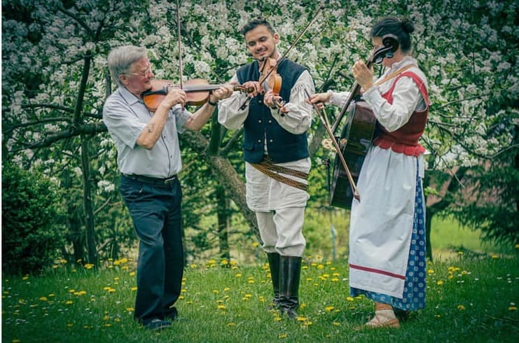 Kobieta i 2 mężczyzn na tle wiosennego ogrodu grają na instrumentach